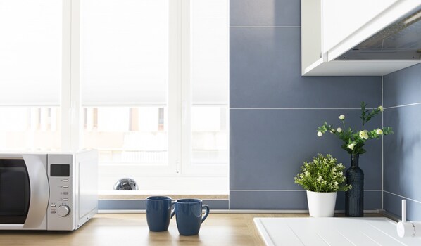 A kitchen with a microwave, two blue mugs, a potted plant, and a white cabinet. - Blue Modern Apartment (Monserrato)