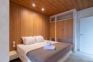 Ein Schlafzimmer mit Holzboden, einem Bett mit weißer Bettwäsche, einem zusammengerollten Handtuch auf dem Bett und eingebauten Schränken.