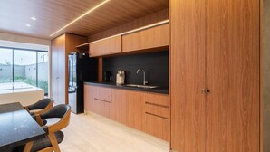 A modern kitchen with wooden cabinets, a black countertop, and a dining area with a table and chairs. - Modern House: 3 Suites | Jacuzzi | 450m from Beach (Florianópolis)