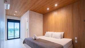 A modern bedroom with a large bed, wooden ceiling, and a view through a sliding door. - Modern House: 3 Suites | Jacuzzi | 450m from Beach (Florianópolis)