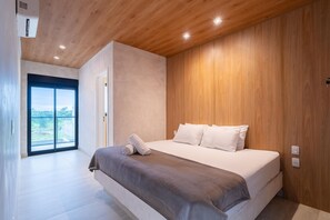 A modern bedroom with a large bed, wooden ceiling, and a view through a sliding door.