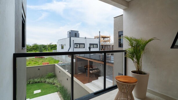 A balcony with a view of a modern building, a potted plant, and a wooden stool. - Modern House: 3 Suites | Jacuzzi | 450m from Beach (Florianópolis)