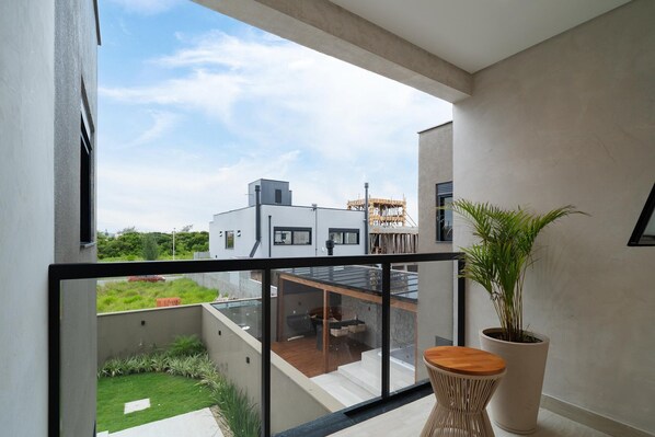 A balcony with a view of a modern building, a potted plant, and a wooden stool.