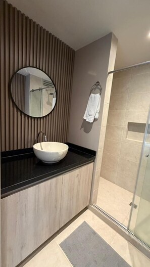 A modern bathroom with a round mirror, a sink, and a shower area. - Santorini Apartamentos amoblados (Pereira)