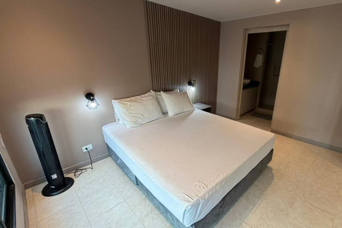 Ein modernes Hotelzimmer mit einem großen Bett, einem Heizkörper, einer Wandleuchte und einer Tür zu einem Badezimmer.