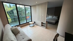 Une chambre d’hôtel moderne dotée d’une grande fenêtre, d’un canapé, d’une petite table ronde, d’un lit et d’un panneau en bois vertical.