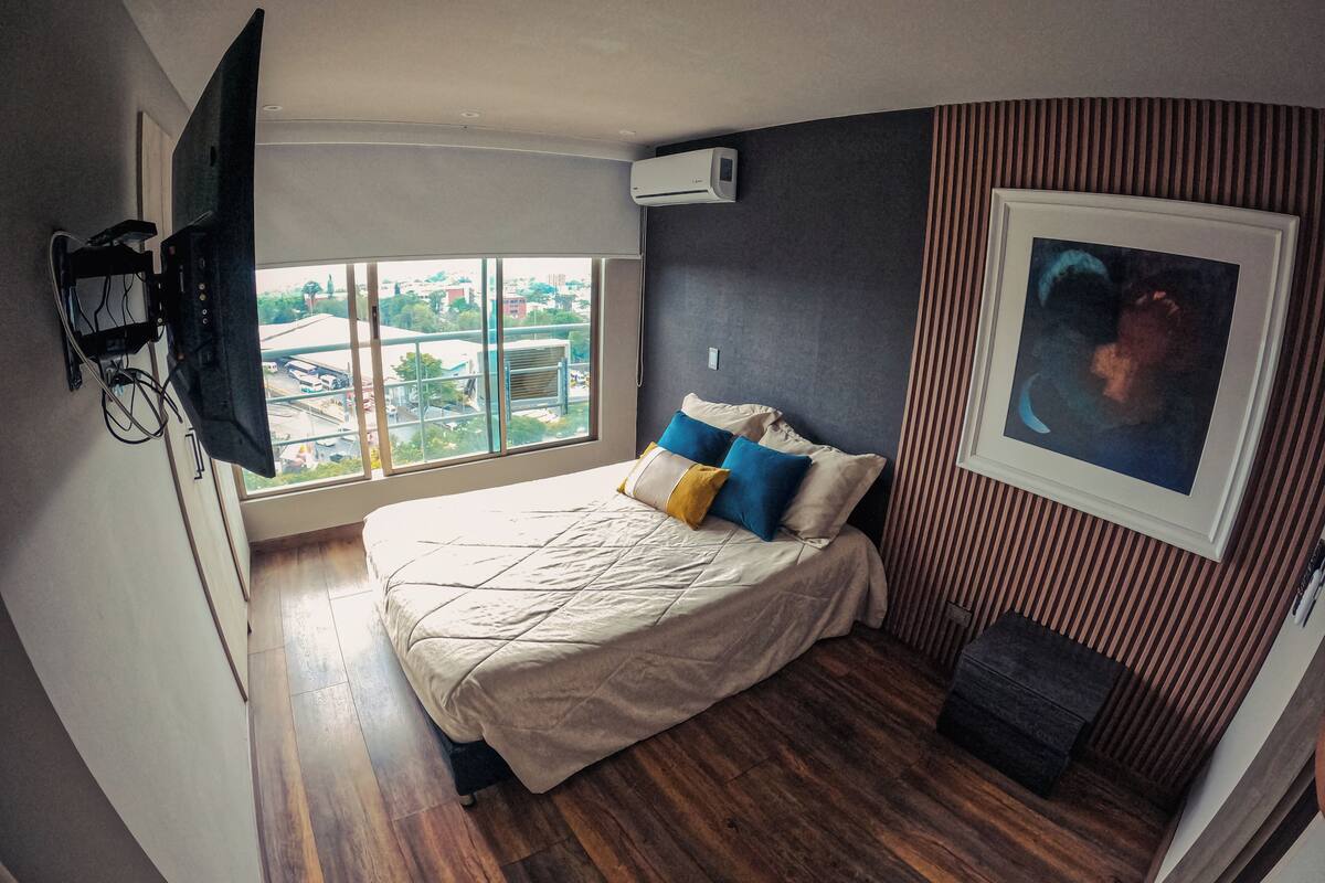 Ein Schlafzimmer mit Bett, Fernseher, Klimaanlage, Fenster mit Blick und einem gerahmten Bild an der Wand.