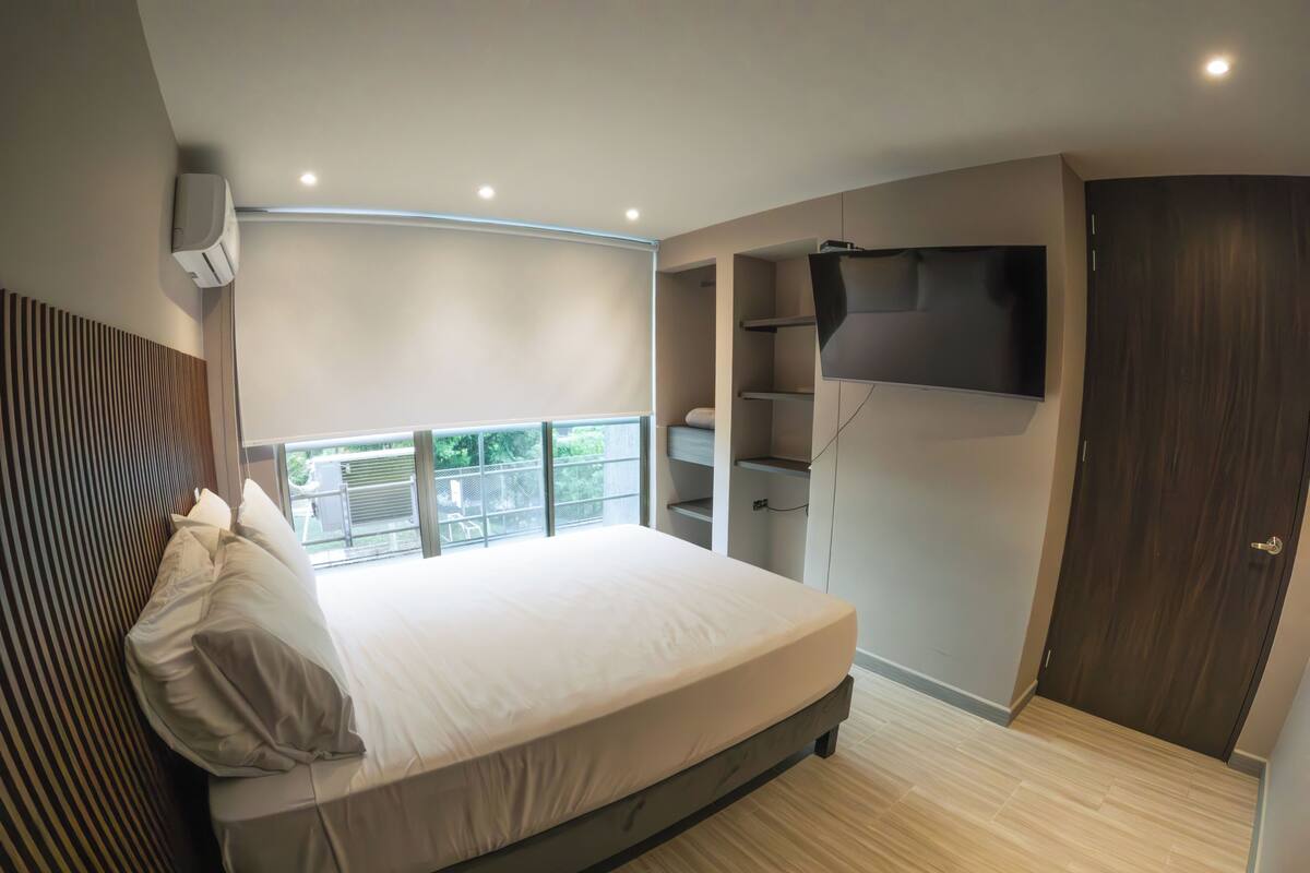 Ein modernes Schlafzimmer mit einem großen Bett, Einbauschränken, einem Flachbildfernseher und einem Balkon.