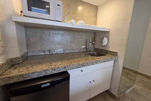 Uma cozinha compacta com bancada de granito, micro-ondas embutido, pia e lava-louças.