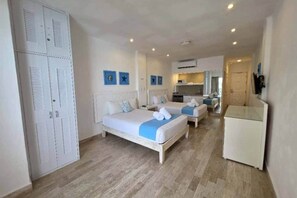 Quarto de hotel com uma cama grande, uma cama menor, uma cozinha compacta e um guarda-roupa.