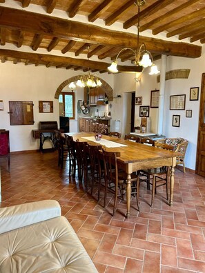 A rustic kitchen with exposed wooden beams, a large dining table, and a cozy seating area with a cushioned bench.
