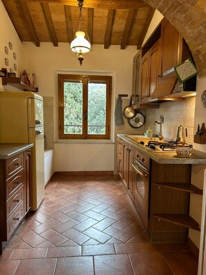 A kitchen with wooden cabinets, a gas stove, a window, and a herringbone-patterned floor.