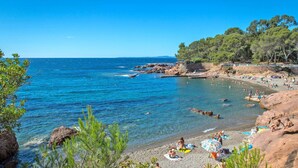 Une plage avec une eau d’un bleu limpide, un rivage rocheux et des gens qui prennent un bain de soleil.