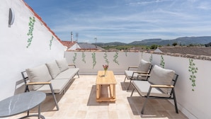 Una terraza con sofá, sillas, una mesa y vistas a colinas distantes.