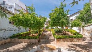 Un patio con una fuente central, escalones de piedra que conducen a un nivel superior y árboles a lo largo del sendero.