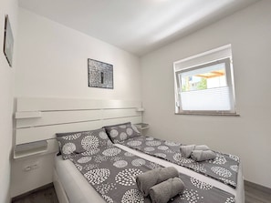 A single bed with a headboard, a small window with blinds, a wall-mounted artwork, and a power outlet. - Sea View Apartment Mariana (Preko)