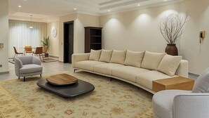 Ein modernes Wohnzimmer mit einer Couch, Sesseln, einem Couchtisch und einem Essbereich im Hintergrund.