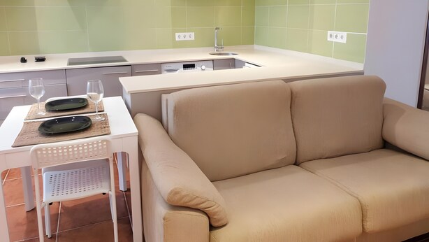 A modern kitchen with a sofa, a dining table with plates and glasses, and a TV above the counter. - Apartment 'Garro1' with Mountain Views (Donostia / San Sebastián)