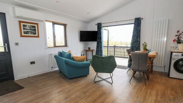 A living room with a sofa, a green chair, a TV, and a dining area with a table and chairs. - Grass Roots (Templecombe)
