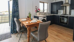 A modern kitchen with a dining area, a built-in washing machine, and a view through the open door. - Grass Roots (Templecombe)