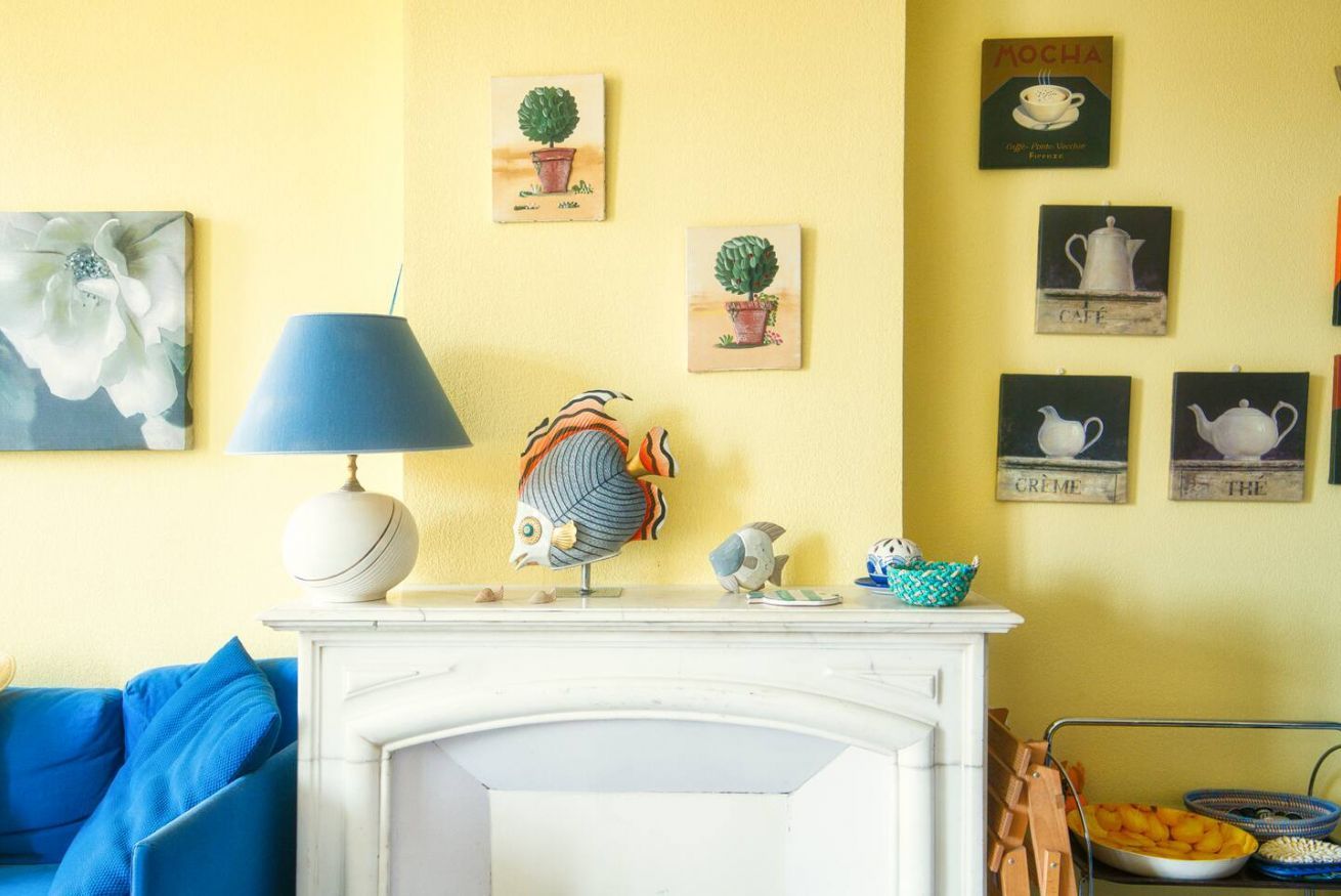 Une pièce avec une cheminée blanche, une lampe bleue et des œuvres d’art murales, notamment une sculpture de poisson et des images sur le thème du café.