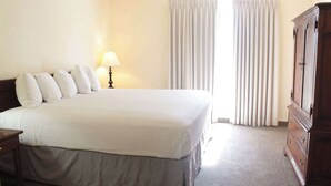 Ein Hotelzimmer mit einem großen Bett, einem Nachttisch, einer Lampe, einem Kleiderschrank und einem Fenster mit Vorhängen.