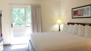 Een hotelkamer met een bed, een lamp, een schilderij en uitzicht op groen.