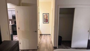 Ein Schlafzimmer mit Bett, Schminktisch und Kleiderschrank. Ein Flur führt zu einer Küchenzeile.