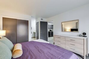 A bedroom with a bed, a dresser, a mirror, and a door leading to a bathroom. - One Bedroom, First Floor (Wichita)