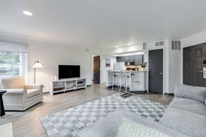 Un salon moderne avec un téléviseur à écran plat, un canapé et un coin repas, avec une cuisine en arrière-plan.
