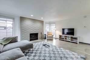 A modern living room with a fireplace, a sofa, a TV, and a patterned rug. - One Bedroom, First Floor (Wichita)