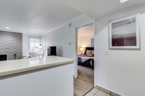 Une cuisine moderne dotée d’un grand îlot central, d’un coin repas avec des chaises et d’une vue sur une chambre à coucher, visible à travers une porte ouverte.