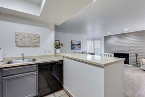 A modern kitchen with a dishwasher, a sink, and a dining area with a fireplace. - One Bedroom, First Floor (Wichita)