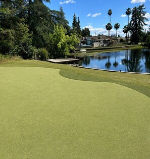 A golf course with a water hazard, trees, and a house in the background. - Lovely Lakeside Home: Perfect for Vacations, Weddings, Retreats. (Clovis)