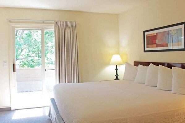 Een hotelkamer met een bed, een nachtkastje, een lamp, een lijst met een foto aan de muur en een deur naar een balkon.