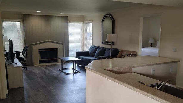 A spacious living area with a fireplace, a dining area, and a kitchen with a built-in island. - Two Bedroom First Floor (Wichita)
