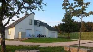 Een huis met twee verdiepingen, een schuin dak, een garage en een voortuin met een haag.