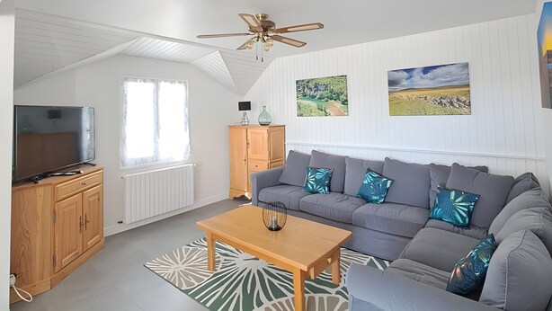 Een moderne woonkamer met een grijze bank, een houten salontafel en een plafondventilator.