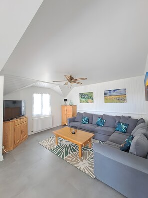 A modern living room with a grey sofa, wooden coffee table, and ceiling fan. - Gîte chez Léon at the Gateway to Aubrac (Peyre en Aubrac)