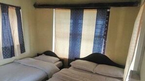 A room with two single beds, a window with curtains, and a wooden ceiling.