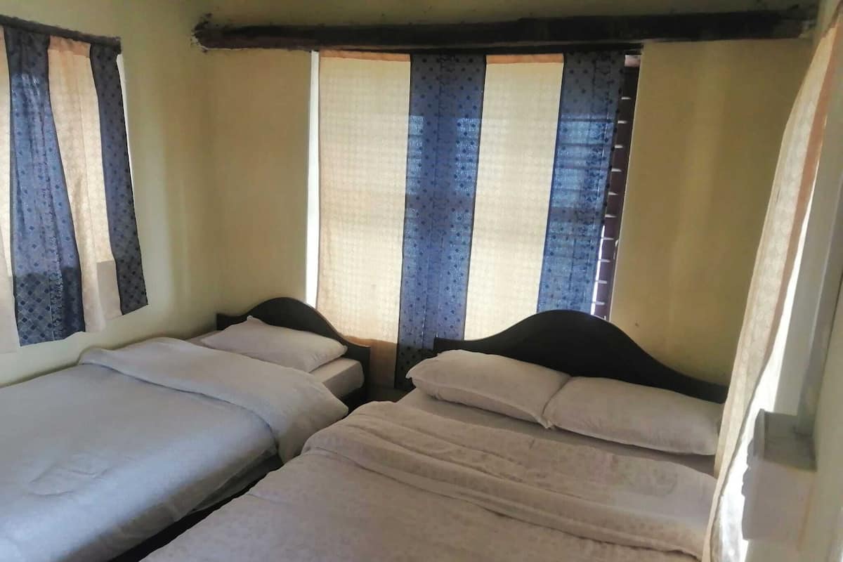 Una habitación con dos camas individuales, una ventana con cortinas y techo de madera.
