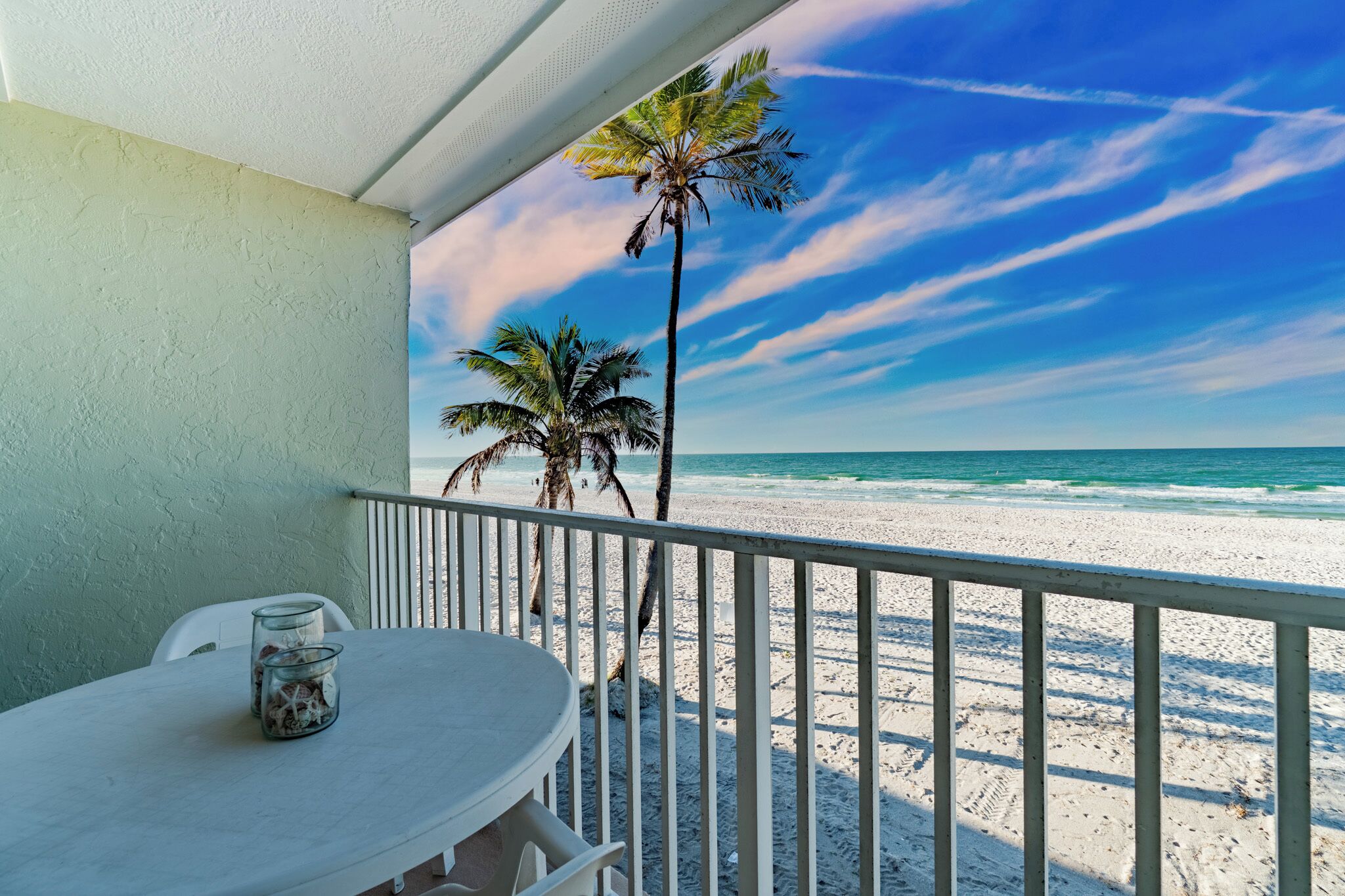 Ein Balkon mit Blick auf den Strand, ein Tisch mit Stühlen und eine Palme.