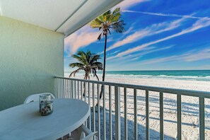 A balcony with a view of the beach, a table with chairs, and a palm tree. - Nautilus 209 by Nautilus Vacations - Beachfront Condo, Pool, Recreation Court (Holmes Beach)