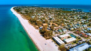An aerial view of a coastal town with a long sandy beach, residential buildings, and a clear blue sky. - Nautilus 209 by Nautilus Vacations - Beachfront Condo, Heated Pool, Racket Court (Holmes Beach)