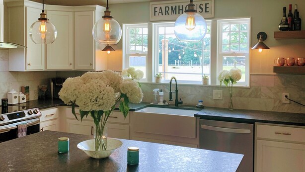 A kitchen with white cabinets, a farmhouse sign, hanging pendant lights, and a vase with flowers on the island. - Charming Country Get-away! Pet Friendly (Fairview)