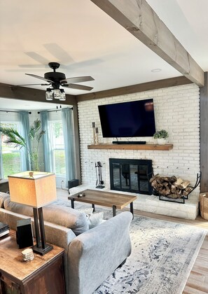 Un salon avec une cheminée, un téléviseur à écran plat, un ventilateur de plafond et un canapé.