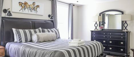 Un dormitorio con cama, ventilador de techo, cómoda, espejo y un cuadro en la pared.