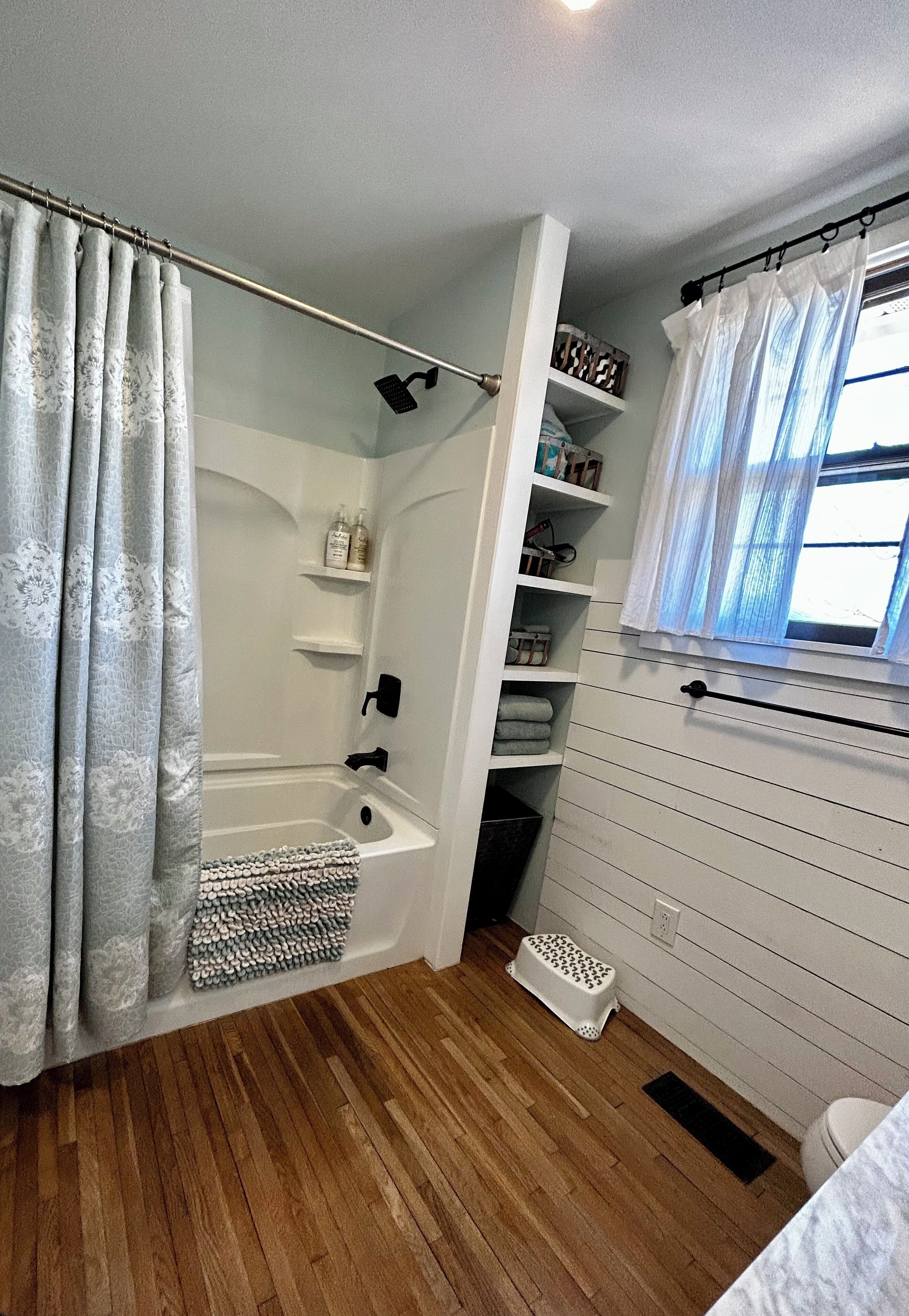 A bathroom with a shower, a toilet, a sink, and a window with curtains.