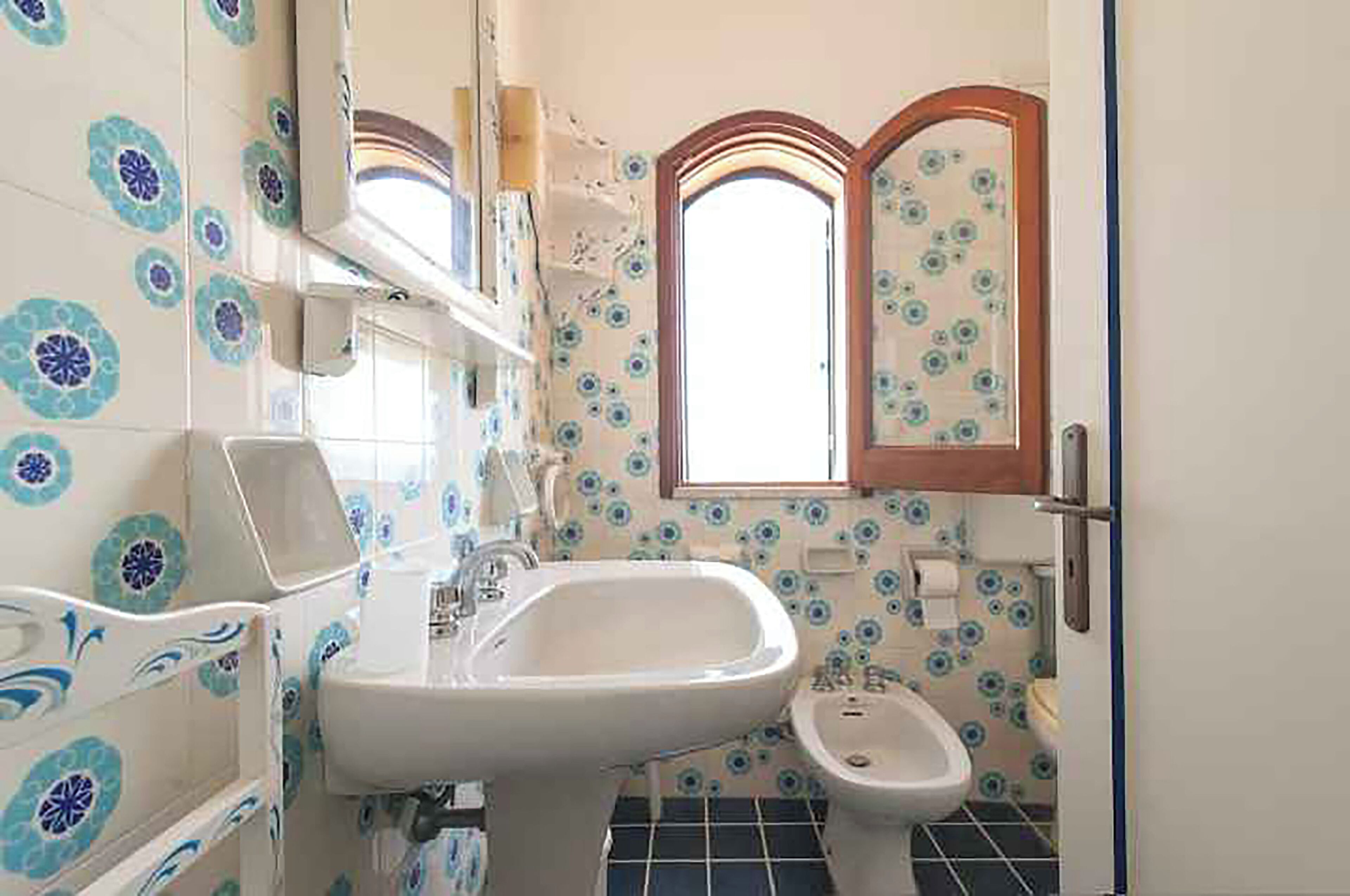 A bathroom with a sink, bidet, and a window with a decorative frame.