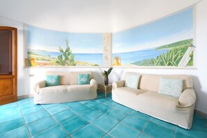 Ein Zimmer mit zwei Sofas, einem Fliesenboden und einem großen Wandbild von einer Küstenlandschaft.